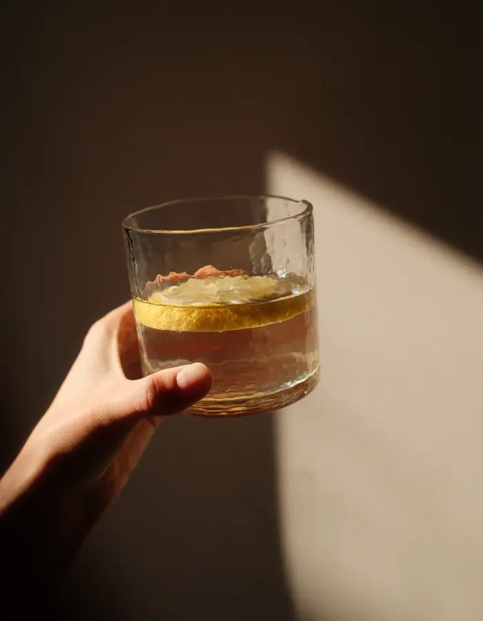 Hand holding a glass of water with lemon in warm sunlight