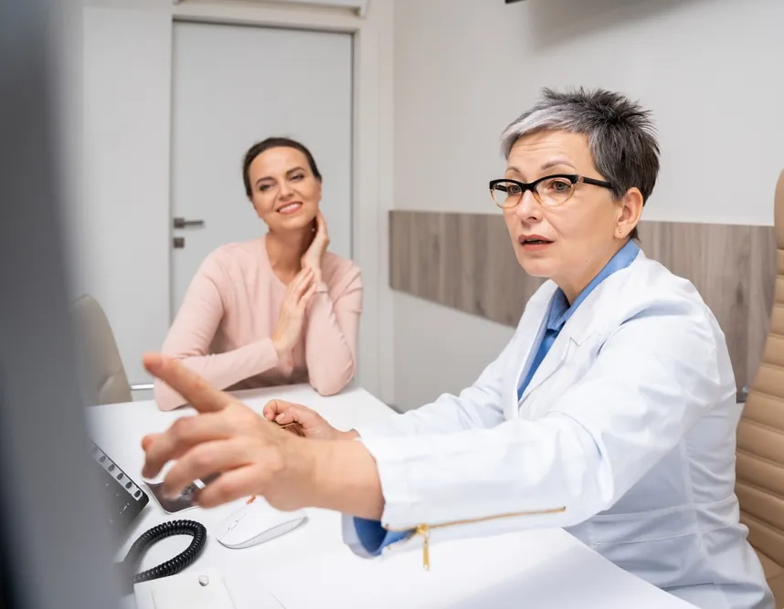 Provider in a white coat pointing to a computer screen while talking with a smiling woman during a hormone evaluation consultation