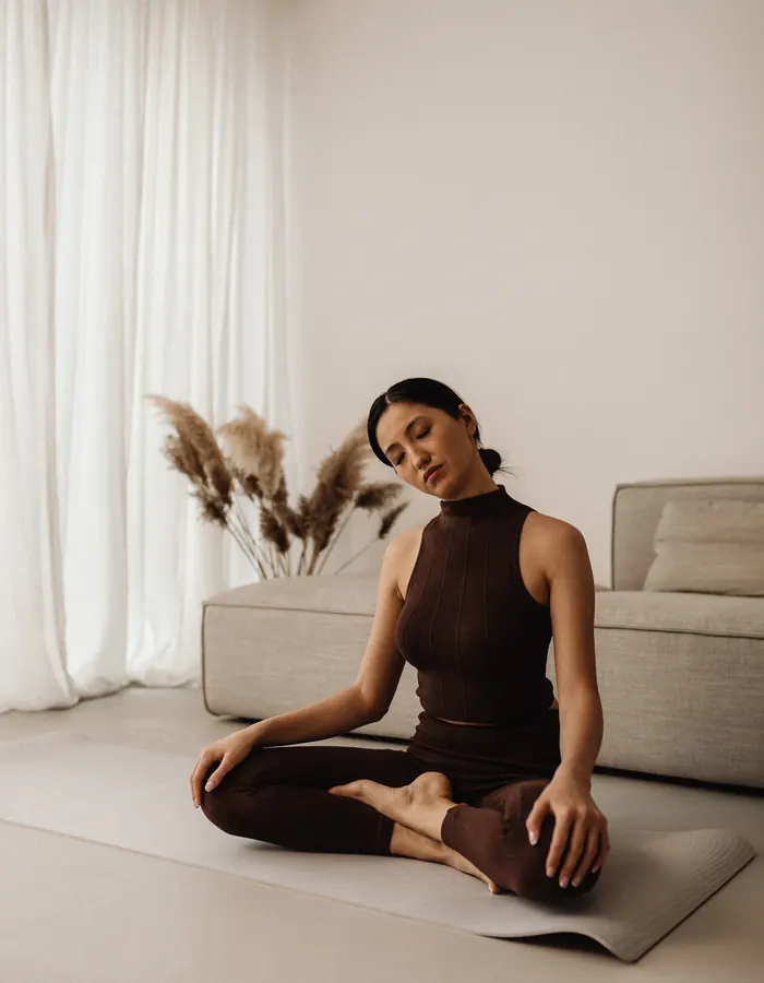 Woman sitting cross-legged on a yoga mat in a calm, neutral living room