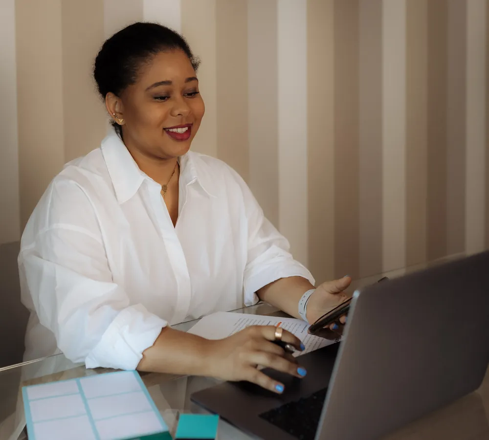 Smiling woman at a desk with a laptop and notes during a hormone replacement therapy consultation